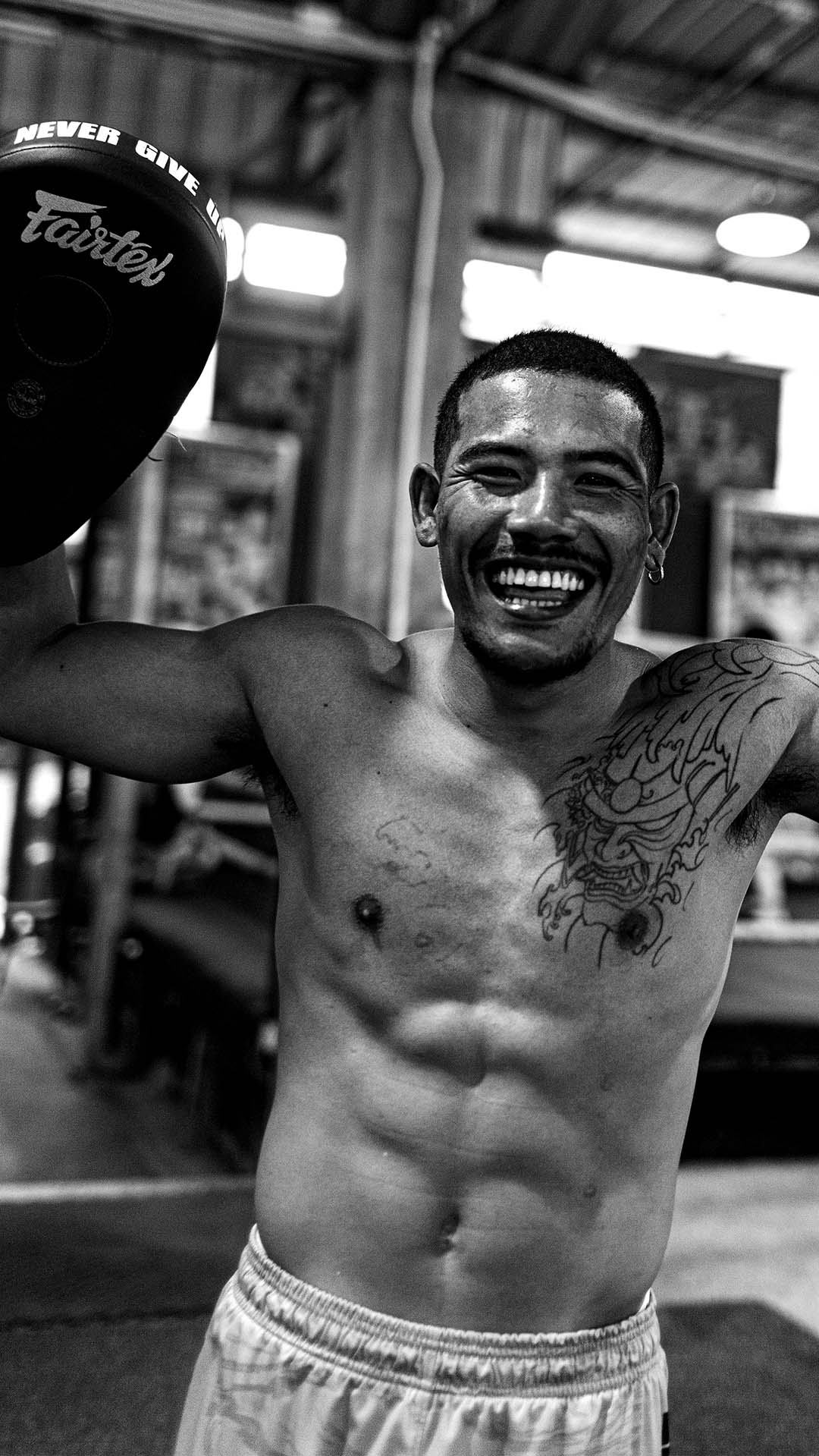 Muay Thai coach smiling while holding pads during training at Rambong Muay Thai Gym